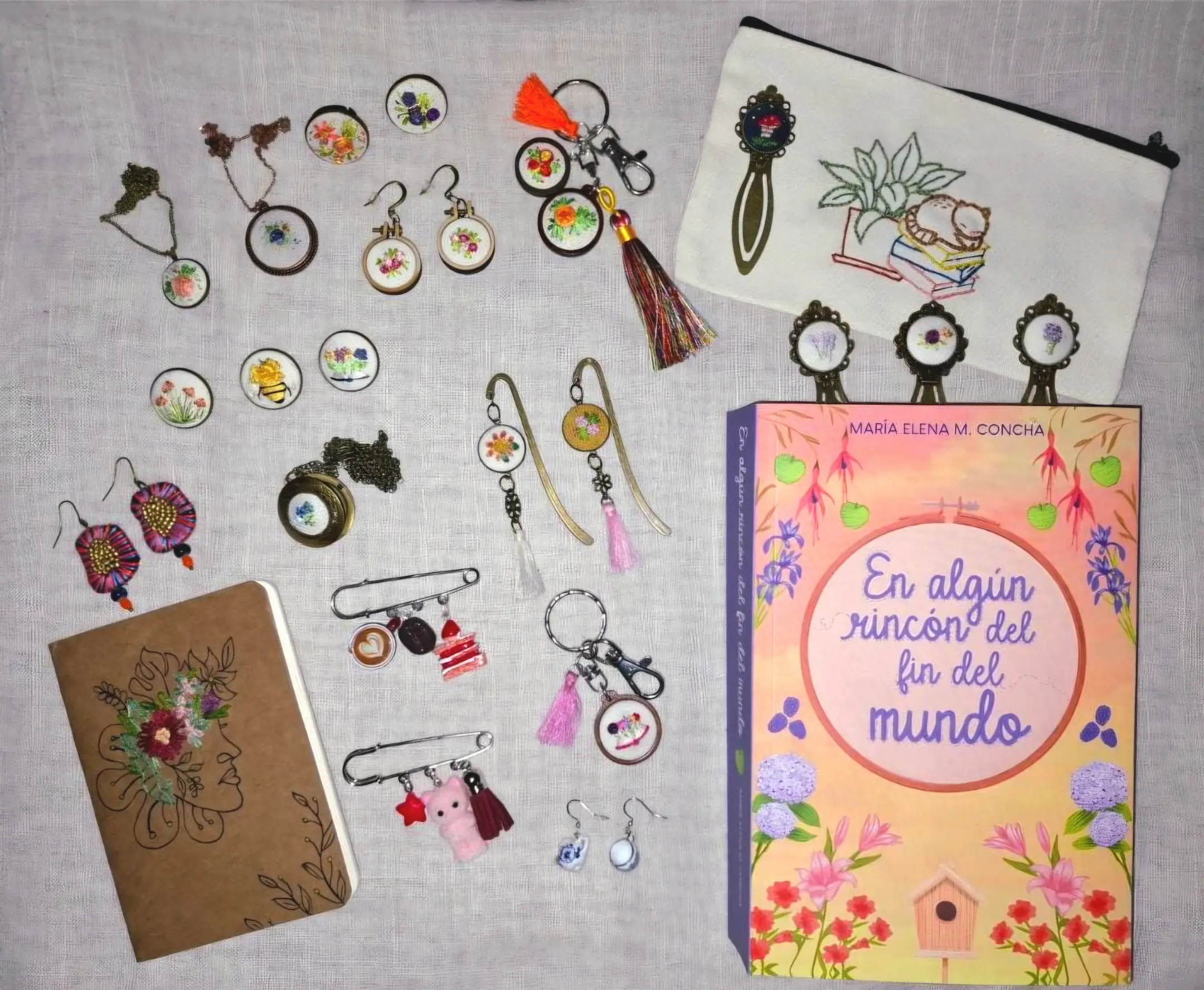Bodegón artesanal de Ralea con la novela "En algún rincón del fin del mundo", marcapáginas bordados a mano y joyería texturada sobre lino.